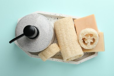Photo of Natural loofah sponges, cosmetic product and soap on light blue background, top view