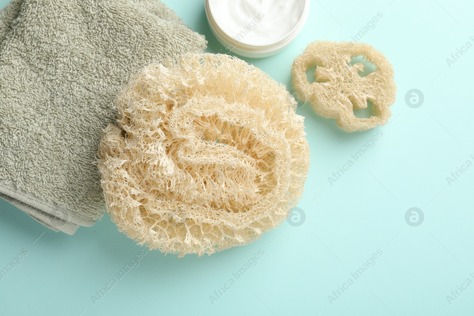 Natural loofah sponges, cosmetic product and towel on light blue background, flat lay. Space for text Photo of Natural loofah sponges, cosmetic product and towel on light blue background, flat lay. Space for text