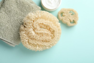 Photo of Natural loofah sponges, cosmetic product and towel on light blue background, flat lay. Space for text