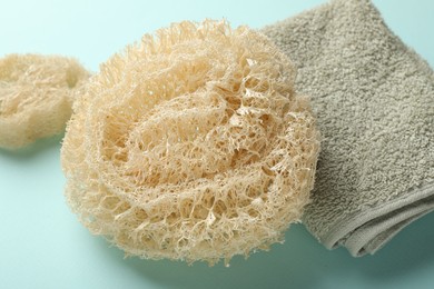 Photo of Natural loofah sponges and towel on light blue background, closeup