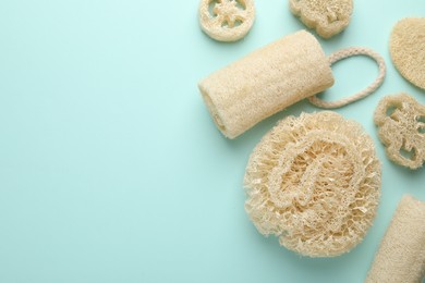 Photo of Natural loofah sponges on light blue background, flat lay. Space for text