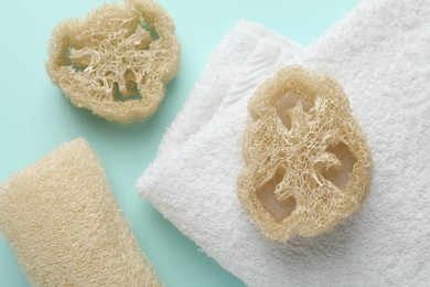 Photo of Natural loofah sponges and towel on light blue background, flat lay