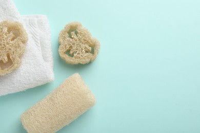 Photo of Natural loofah sponges and towel on light blue background, flat lay. Space for text