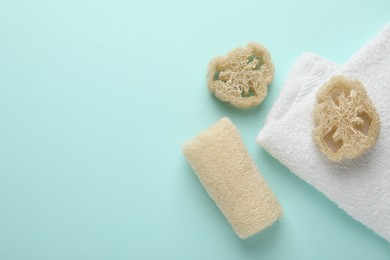 Photo of Natural loofah sponges and towel on light blue background, flat lay. Space for text