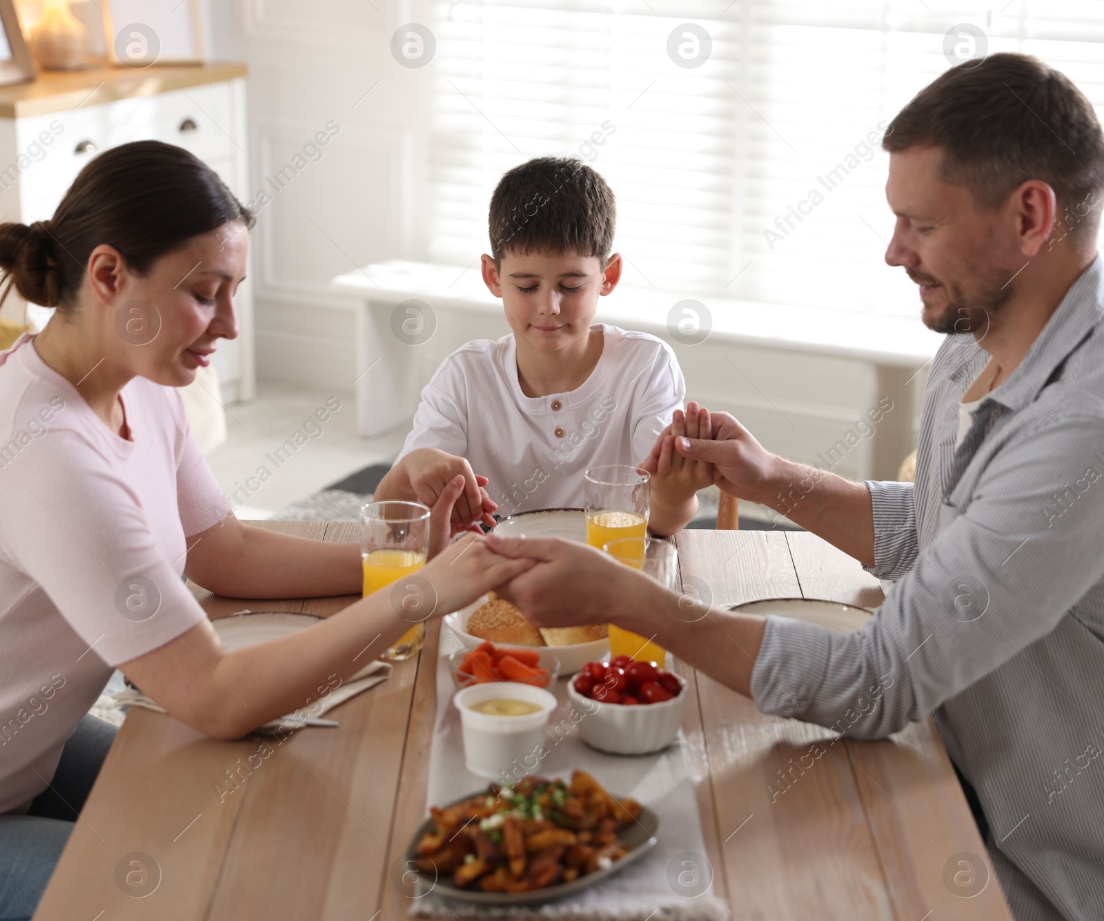 Family praying together before dinner at table indoors Photo of Family praying together before dinner at table indoors