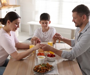 Photo of Family praying together before dinner at table indoors