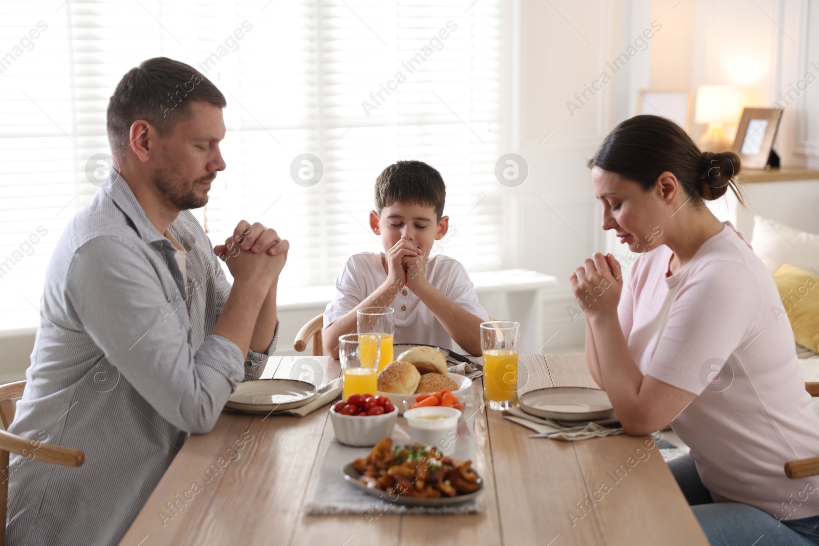 Family praying together before dinner at table indoors Photo of Family praying together before dinner at table indoors