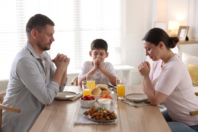 Photo of Family praying together before dinner at table indoors