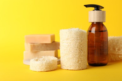 Photo of Natural loofah sponges and cosmetic products on yellow background, closeup