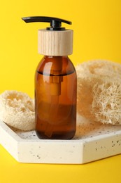 Photo of Natural loofah sponges and cosmetic product on yellow background, closeup