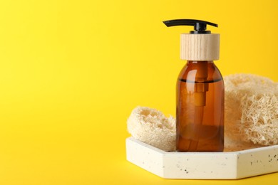 Photo of Natural loofah sponges and cosmetic product on yellow background, closeup. Space for text