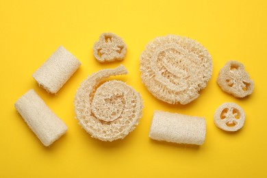 Photo of Natural loofah sponges on yellow background, flat lay