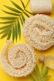 Photo of Natural loofah sponges, cosmetic product and green twigs on yellow background, flat lay