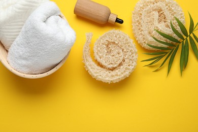 Photo of Natural loofah sponges, cosmetic product, towels and green twig on yellow background, flat lay. Space for text