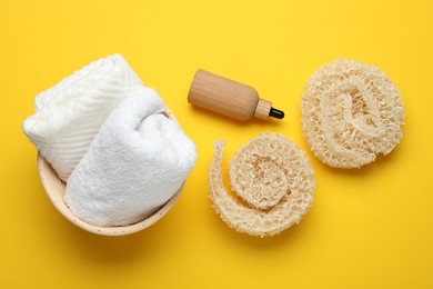 Photo of Natural loofah sponges, cosmetic product and towels on yellow background, flat lay