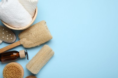 Photo of Natural loofah sponges, cosmetic product, brushes and towels on light blue background, flat lay. Space for text