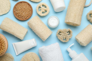 Photo of Natural loofah sponges, cosmetic products, towel and brush on light blue background, flat lay