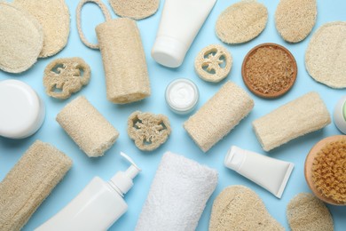 Photo of Natural loofah sponges, cosmetic products, towel and brush on light blue background, flat lay
