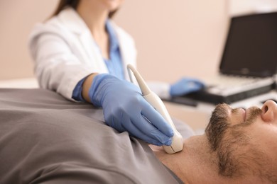 Photo of Sonographer conducting ultrasound examination of man's thyroid gland in clinic, closeup