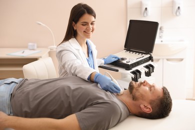 Photo of Sonographer conducting ultrasound examination of man's thyroid gland in clinic