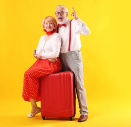 Photo of Lovely senior couple with suitcase on yellow background
