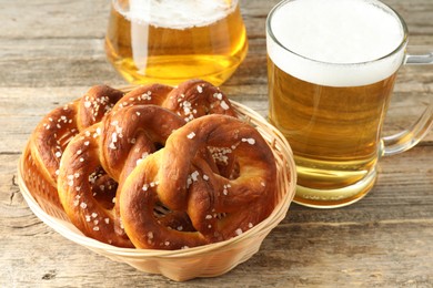 Photo of Tasty pretzels in basket and glasses of beer on wooden table, closeup