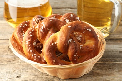 Photo of Tasty pretzels in basket and glasses of beer on wooden table, closeup