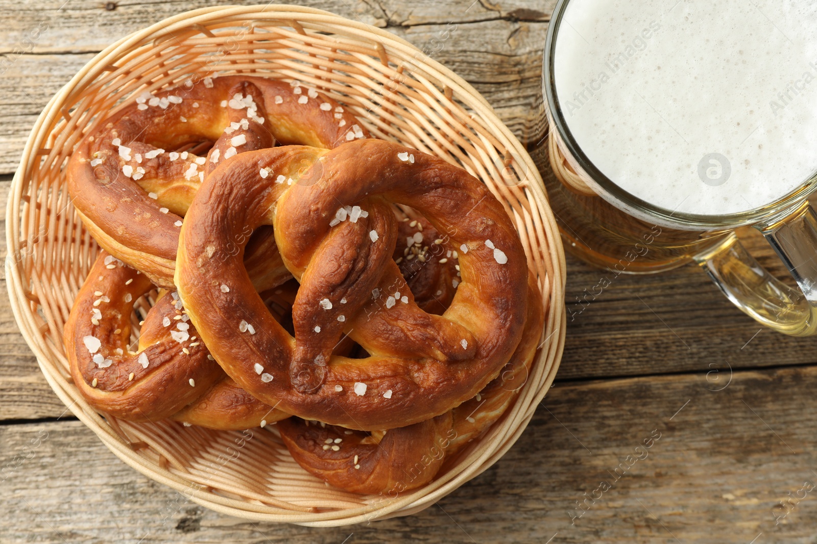 Tasty pretzels in basket and glass of beer on wooden table, flat lay Photo of Tasty pretzels in basket and glass of beer on wooden table, flat lay