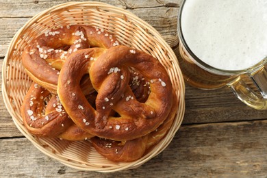 Photo of Tasty pretzels in basket and glass of beer on wooden table, flat lay