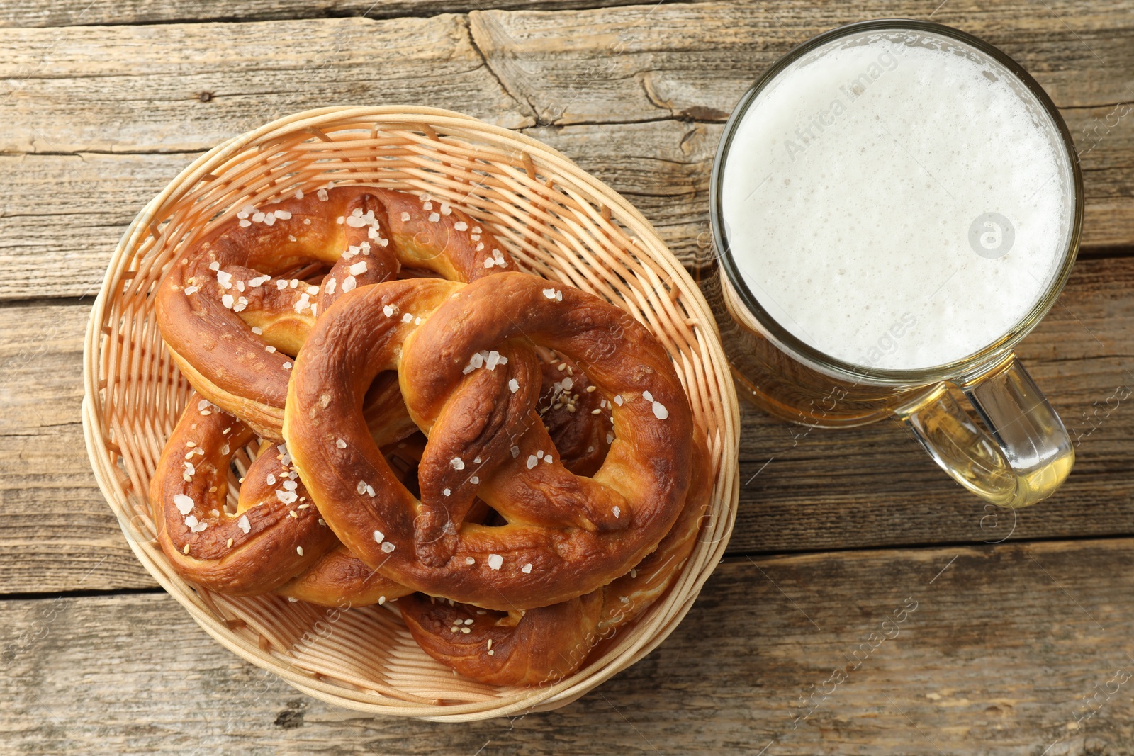 Tasty pretzels in basket and glass of beer on wooden table, flat lay Photo of Tasty pretzels in basket and glass of beer on wooden table, flat lay