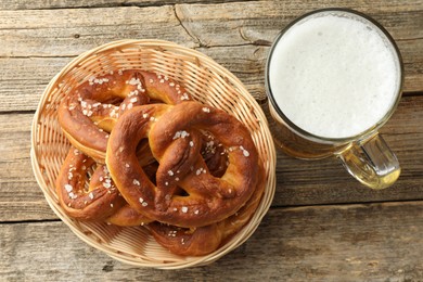 Photo of Tasty pretzels in basket and glass of beer on wooden table, flat lay