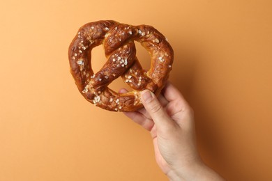 Photo of Woman with tasty pretzel on orange background, closeup