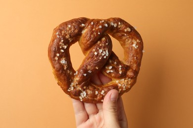 Photo of Woman with tasty pretzel on orange background, closeup