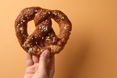 Photo of Woman with tasty pretzel on orange background, closeup. Space for text