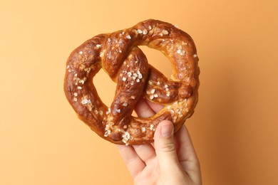 Photo of Woman with tasty pretzel on beige background, closeup