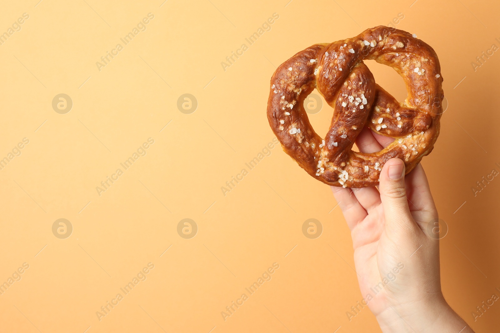 Woman with tasty pretzel on beige background, closeup. Space for text Photo of Woman with tasty pretzel on beige background, closeup. Space for text