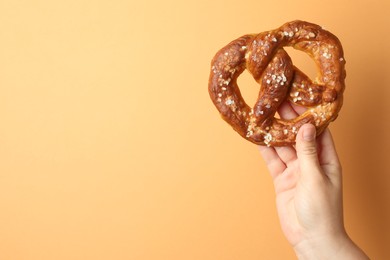 Photo of Woman with tasty pretzel on beige background, closeup. Space for text