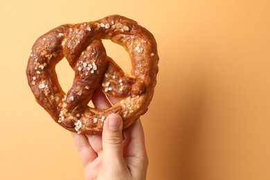 Photo of Woman with tasty pretzel on beige background, closeup. Space for text