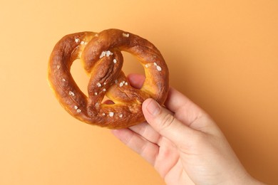 Photo of Woman with tasty pretzel on beige background, closeup