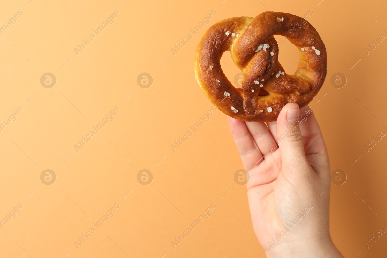 Woman with tasty pretzel on beige background, closeup. Space for text Photo of Woman with tasty pretzel on beige background, closeup. Space for text