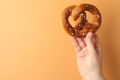 Photo of Woman with tasty pretzel on beige background, closeup. Space for text