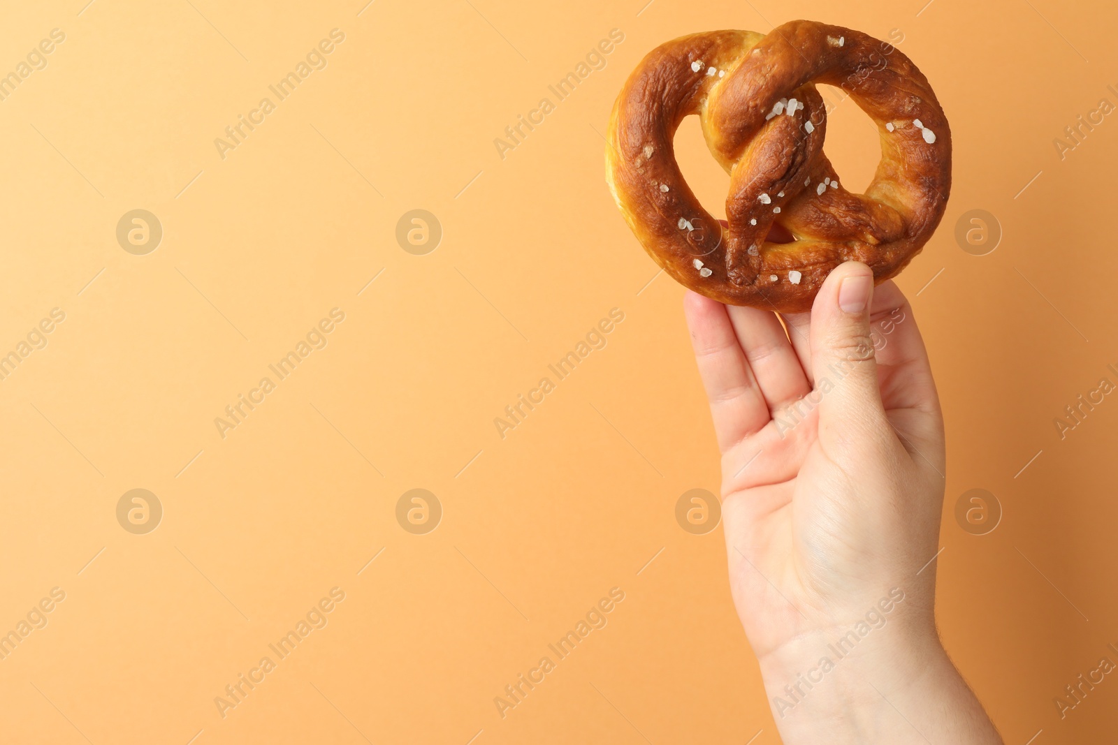 Woman with tasty pretzel on beige background, closeup. Space for text Photo of Woman with tasty pretzel on beige background, closeup. Space for text