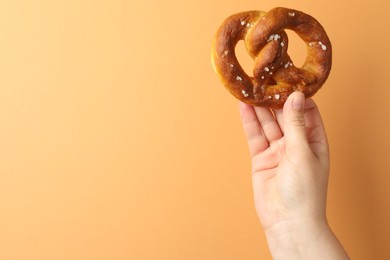 Photo of Woman with tasty pretzel on beige background, closeup. Space for text