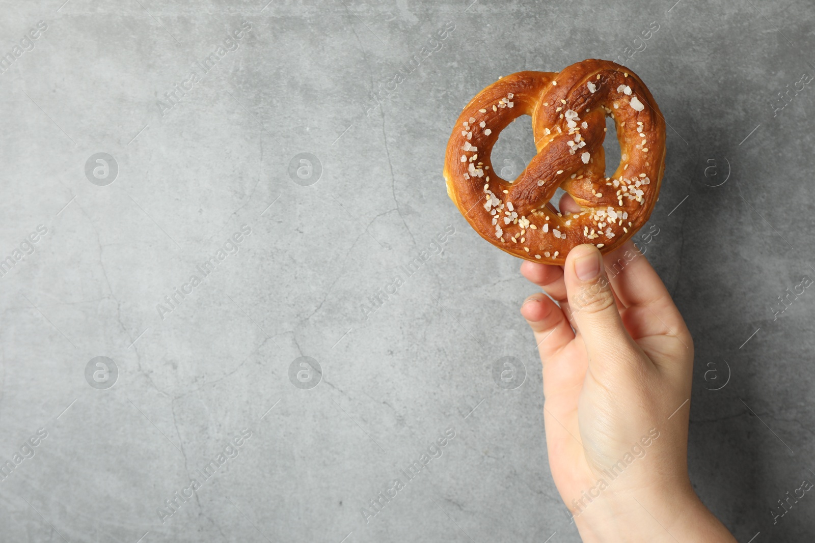 Woman with tasty pretzel near grey textured wall, closeup. Space for text Photo of Woman with tasty pretzel near grey textured wall, closeup. Space for text