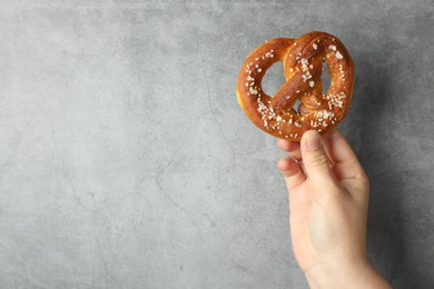 Photo of Woman with tasty pretzel near grey textured wall, closeup. Space for text