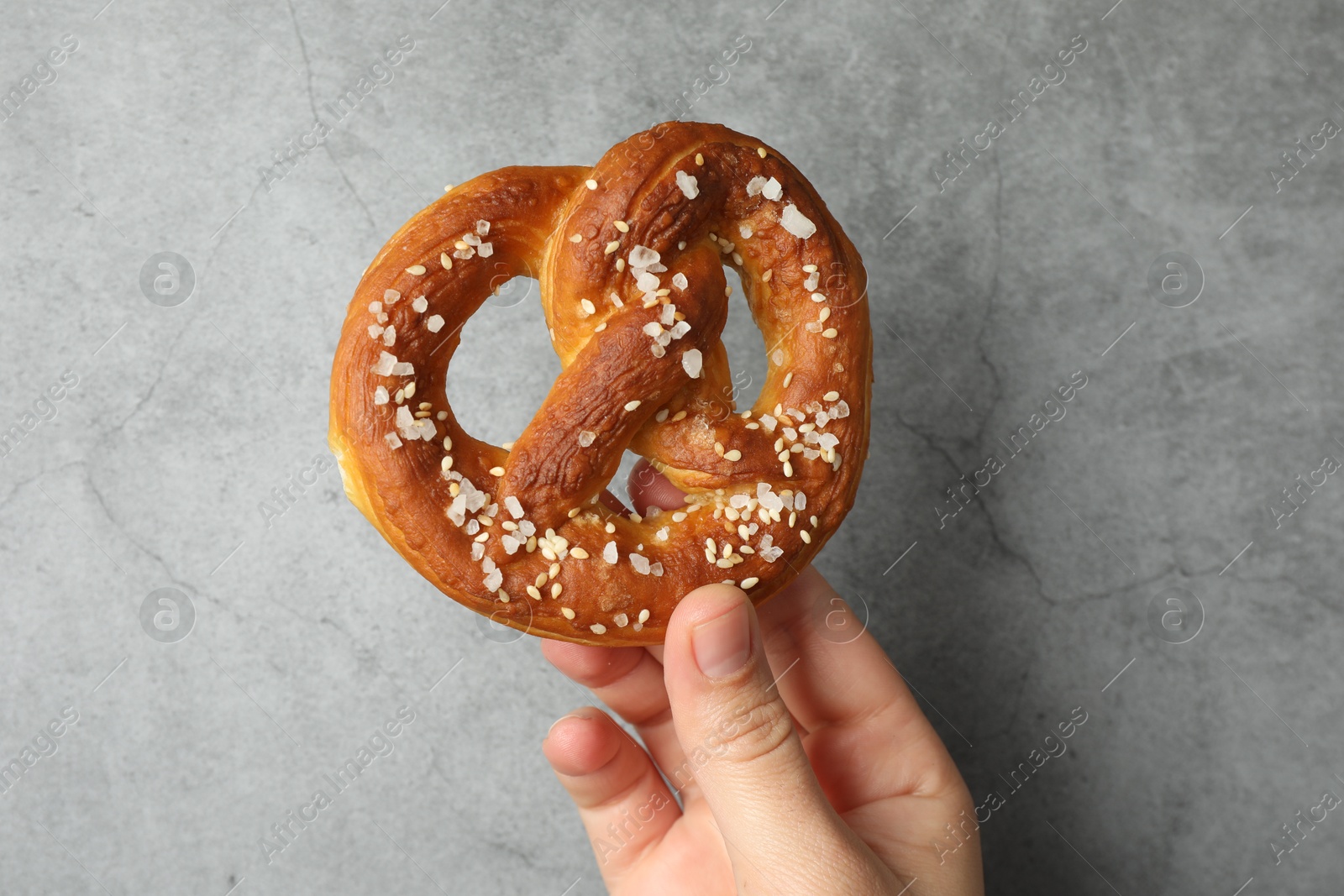 Woman with tasty pretzel near grey textured wall, closeup Photo of Woman with tasty pretzel near grey textured wall, closeup