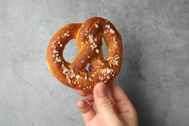Photo of Woman with tasty pretzel near grey textured wall, closeup