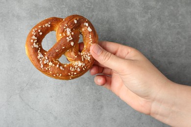 Photo of Woman with tasty pretzel near grey textured wall, closeup