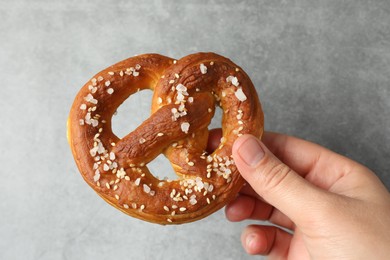 Photo of Woman with tasty pretzel near grey textured wall, closeup
