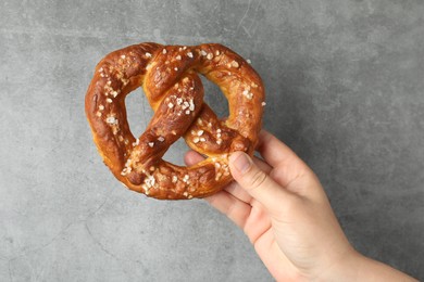 Photo of Woman with tasty pretzel near grey textured wall, closeup